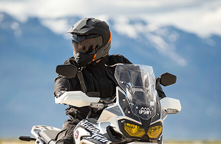 Man riding a upshift bike while wearing a Black and orange gmax helmet Man riding a grey and black bike wearing a black gmax helmet